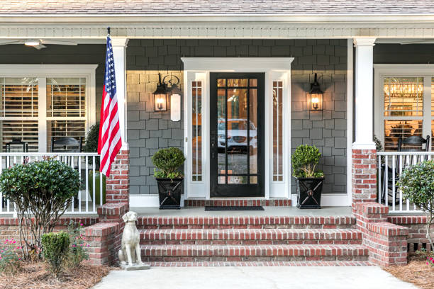 Front door entrance to a large two story blue gray house with wood and vinyl siding and a large American flag. Close up of the front door entrance to a large two story blue gray house with wood and vinyl siding and a large American flag. front door photos stock pictures, royalty-free photos & images