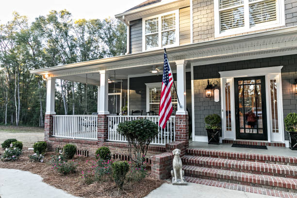 Front door entrance to a large two story blue gray house with wood and vinyl siding and a large American flag. Close up of the front door entrance to a large two story blue gray house with wood and vinyl siding and a large American flag. houses for sale stock pictures, royalty-free photos & images