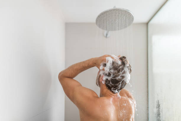 uomo che si lava la doccia lavando i capelli sott'acqua cadendo dal soffione della pioggia in un lussuoso bagno walk-in. doccia giovane a casa stile di vita. routine mattutina di cura del corpo alla luce del sole - washing hair foto e immagini stock