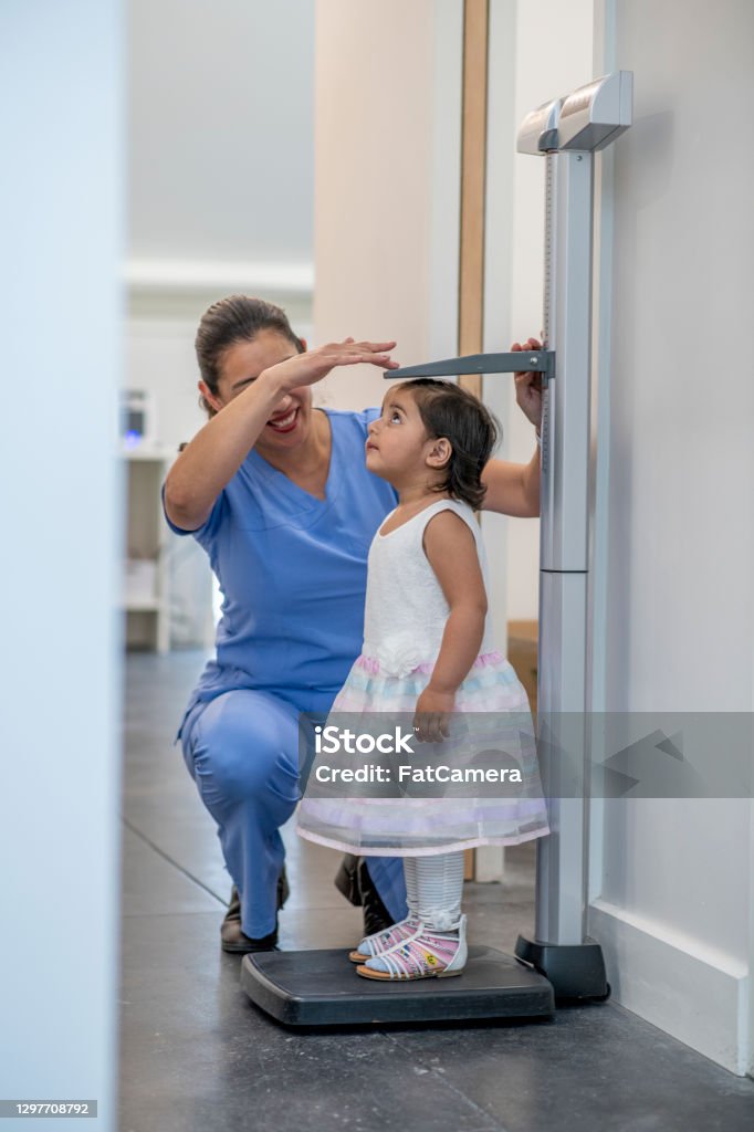 Let's see how much you've grown A female nurse is taking her young patient's height measurement using a stadiometer at the hospital. Child Stock Photo