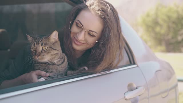 smiling lady with funny tabby cat leans out of car at field