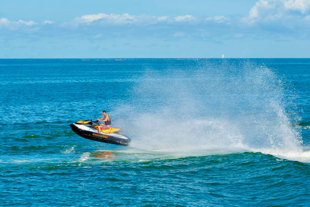 Reedville, Virginia / USA - June 21, 2020: A young man rides a jet ski in the Chesapeake Bay jumping the wake of a ferry boat on a hot summer afternoon.
