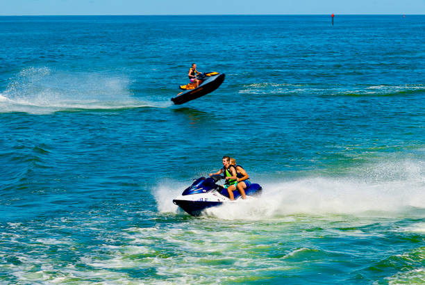 Young Men Jump Waves on a Jetski Reedville, Virginia / USA - June 21, 2020: Two young men in the foreground ride a jet ski in the Chesapeake Bay as their friend “catches air” in the background. jump jet stock pictures, royalty-free photos & images