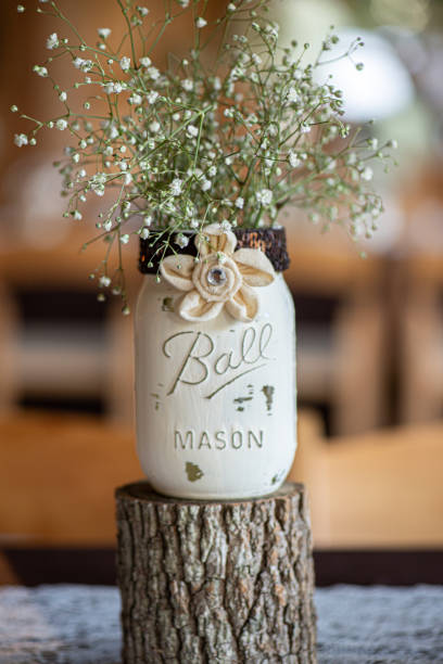 centrotavola in barattolo di muratura bianco con fiori di tele e bambini respirano all'interno su un ceppo di legno - wedding centerpiece foto e immagini stock