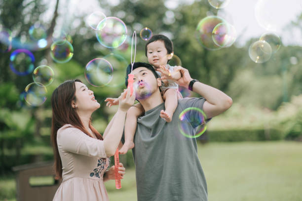 asiática china joven familia jugando burbuja disfrutando de tiempo de picnic al aire libre durante el fin de semana - bubble child bubble wand blowing fotografías e imágenes de stock