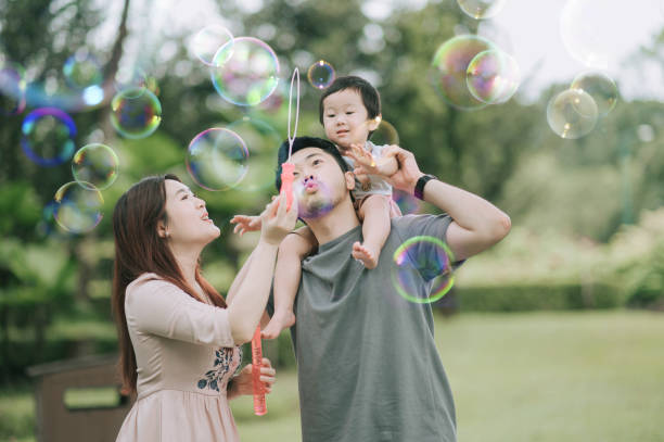 asian chinese young family playing bubble enjoying picnic time outdoor during weekend - bubble child bubble wand blowing imagens e fotografias de stock