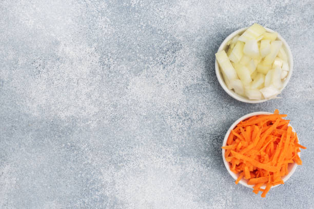 istock Grated carrots and chopped onions in a white plate. Raw vegetables, ingredients for roasting. gray background, copy space, top view. 1297718941
