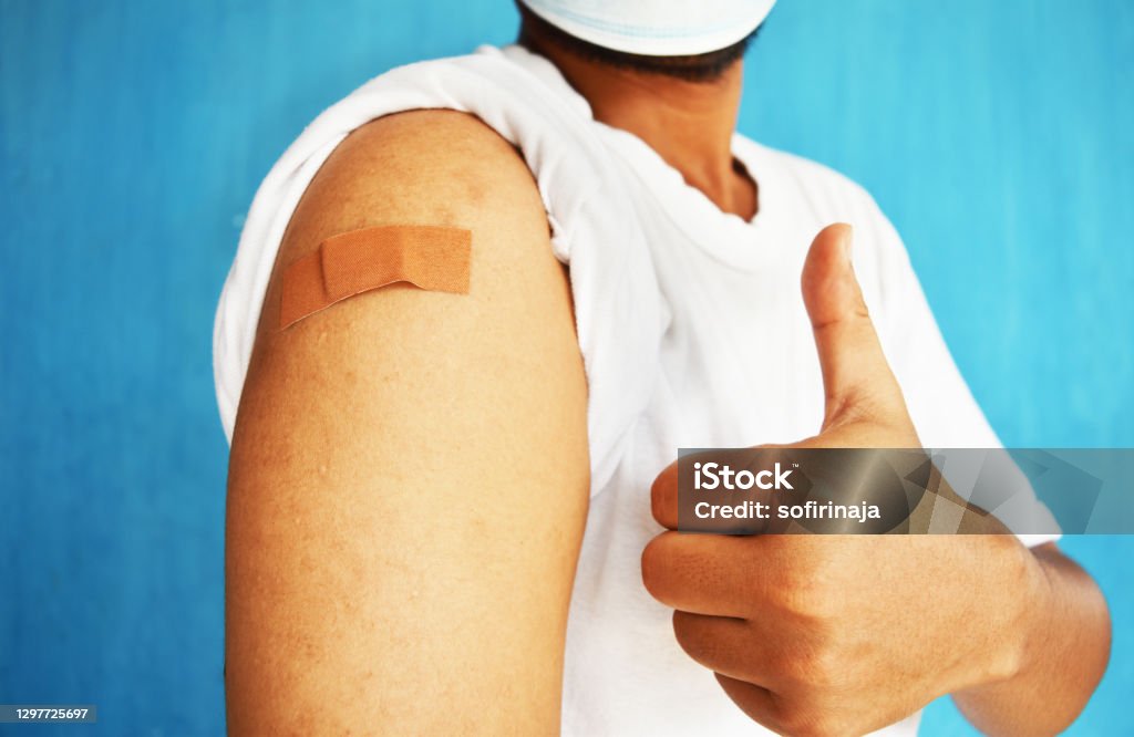 Asian man using adhesive bandage plaster on her arm showing thumb up gesture after injection vaccine. Vaccination Stock Photo