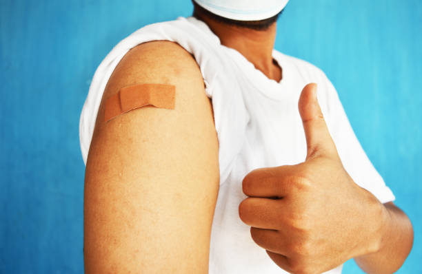 亞洲男子在注射疫苗后，手臂上用膠帶膏膏，露出豎起大拇指的手勢。 - 注射疫苗 個照片及圖片檔