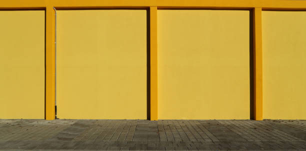 istock Bright yellow wall divided into rectangles by small columns of the same color. Gray concrete tiled pavement under it. 1297727604