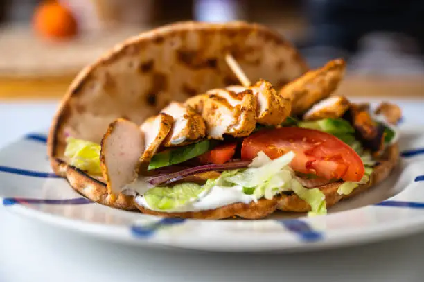 Chicken shawarma in pita bread with vegetable salad on plate on kitchen table, closeup.