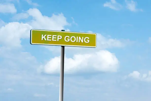 Photo of Keep Going. Road sign against a blue cloudy sky. Achievement of the goal. Achieving success.