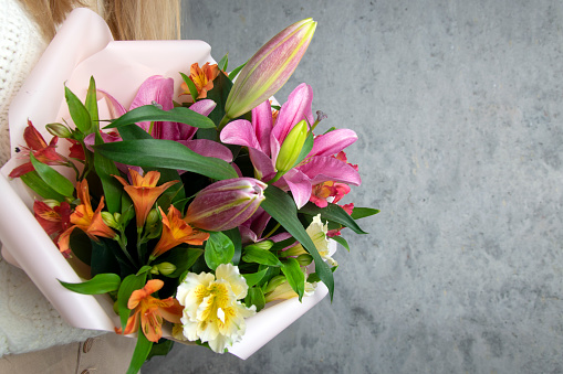 The girl holds in her hands a luxurious bouquet of flowers against the background of a concrete wall.