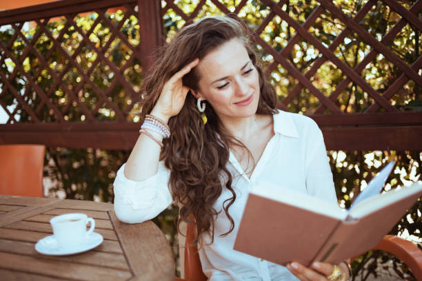 istock relaxed elegant female in shirt sitting at table reading book 1297742679