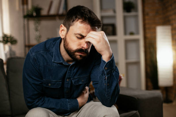 istock Young man sitting on sofa having fever 1297745352