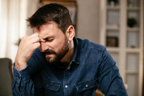 istock Young man sitting on sofa having fever 1297745373