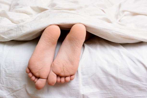 Little female child sleeps in bed and her bare feet are visible from under the blanket Pair of little girl`s feet in a bed young soles stock pictures, royalty-free photos & images