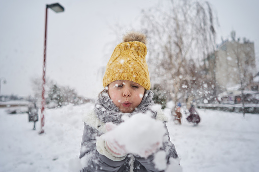 Adorable and excited 5-year-old girl enjoying the winter day while snowing, playing with a snowball