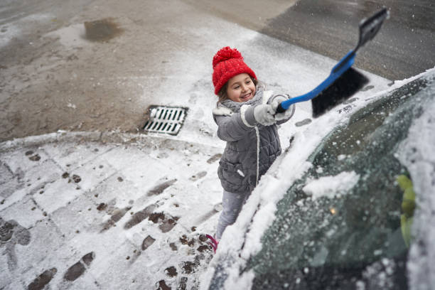 istock Playful 5-year-old girl using a plastic ice scraper to remove the snow from the car 1297760733