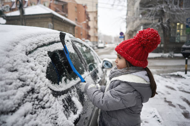 ciekawa dziewczyna czyszczenia samochodu ze śniegu z plastikowym skrobakem lodu - snow car window ice scraper zdjęcia i obrazy z banku zdjęć