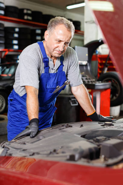 istock Pensive elderly man mechanic looking at car in auto workshop, determining scope of work 1297762435
