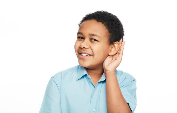 il ragazzo afroamericano tiene la mano vicino all'orecchio per ascoltare, isolato su sfondo bianco. concetto di test dell'udito - young ears foto e immagini stock