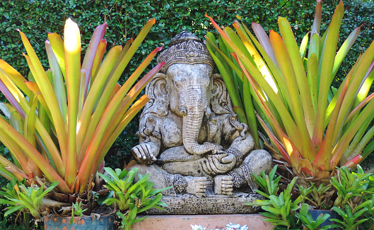 Stone sculpture of the Indian god Ganesha among the greenery in the park of Thailand