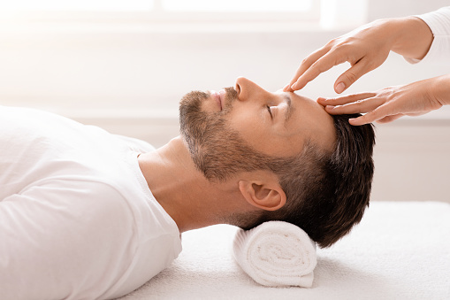 Unrecognizable masseuse hands rubbing sleeping middle-aged man forehead, making relaxing head massage, closeup. Handsome businessman attending spa salon, getting face massage, side view