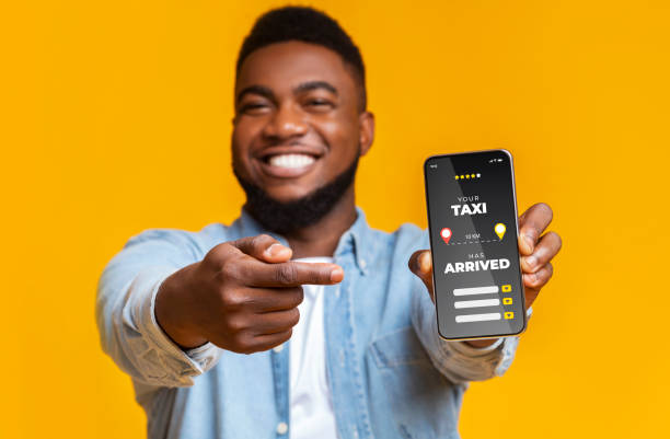 istock Joyful Black Guy Pointing At Smartphone With Opened Taxi Rate App 1297766015