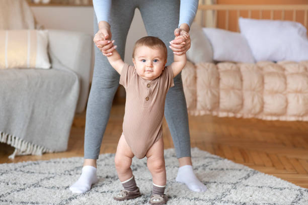 istock Cute baby taking first steps with mother help, home interior 1297769271