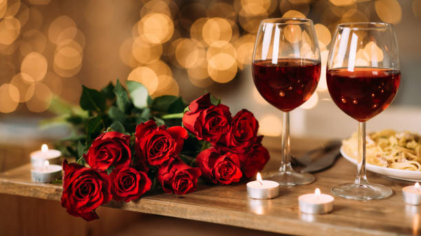 Roses, two glasses of red wine and candles on desk Romantic Dinner. Bouquet of flowers lying on the table, selective focus on bunch of roses, two glasses of red wine and candles on the wooden desk. Date concept, blurred background, banner, copy space valentines day stock pictures, royalty-free photos & images