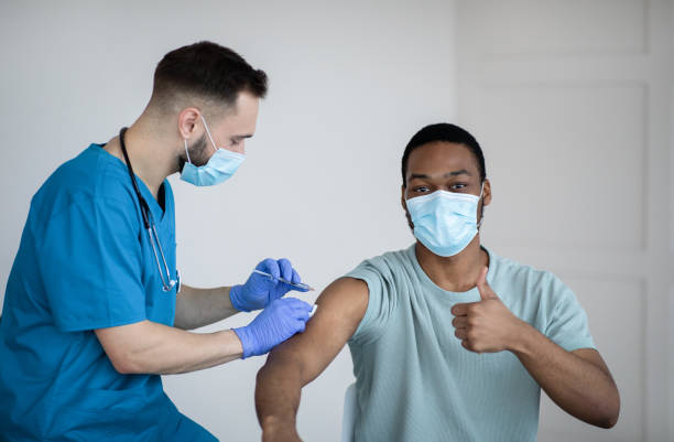 istock Black guy in face mask gesturing thumb up during covid-19 vaccination, approving of coronavirus immunization campaign 1297770505