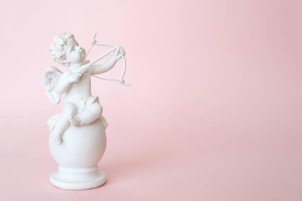 statuetta di un angelo cupido con un fiocco su sfondo rosa. san valentino - cupid foto e immagini stock