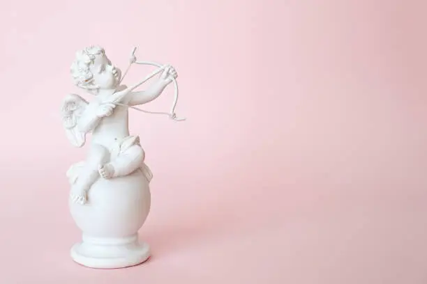 Photo of figurine of an angel Cupid with a bow on a pink background. Valentine's Day