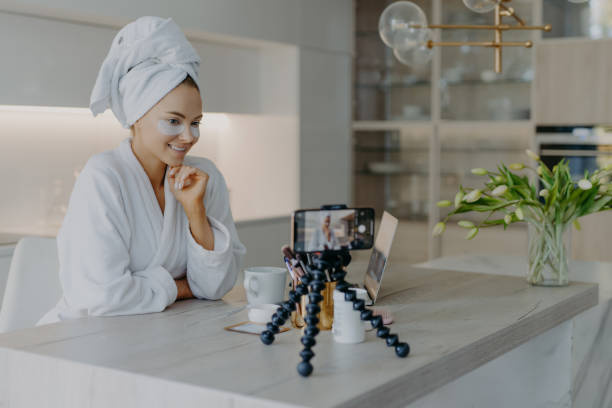 istock Beautiful successful female blogger records tutorial video talks with followers looks at camera of smartphone on tripod applies beauty patches under eyes dicuss how to care about skin and complexion 1297773054