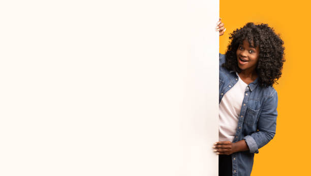 istock Amazed stylish african lady looking at blank advertisement board 1297773525