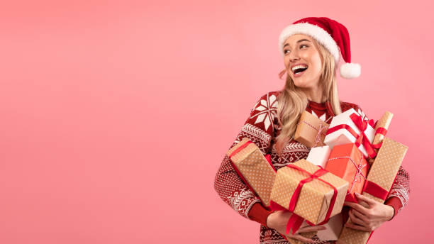 산타 모자와 크리스마스 스웨터에 행복한 밀레니엄 여성은 분홍색 배경에 선물 상자의 더미를 들고, 배너 디자인 - xmas shopping 뉴스 사진 이미지