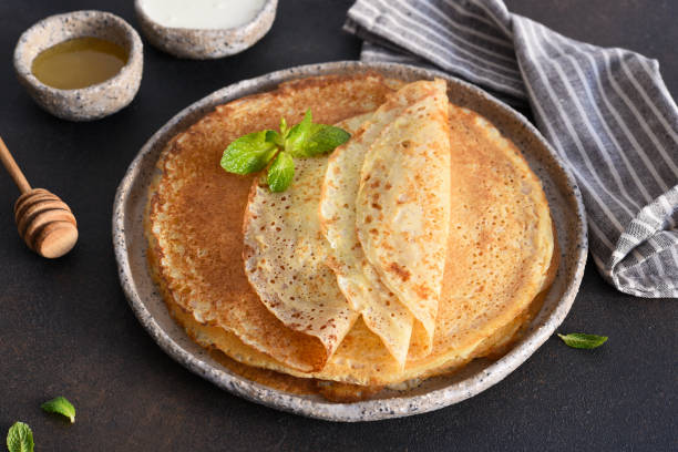 Thin pancakes with sour cream and honey on a dark concrete background. Stack of pancakes. Thin pancakes with sour cream and honey on a dark concrete background. Stack of pancakes. crêpe pancake stock pictures, royalty-free photos & images
