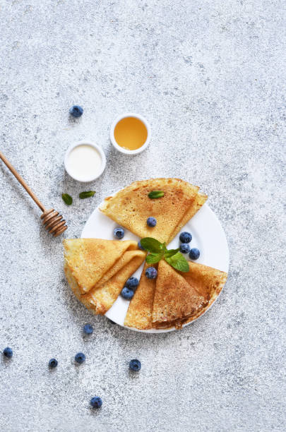 istock Thin pancakes with sour cream, honey and blueberries on a dark concrete background. A stack of pancakes. View from above. 1297776287