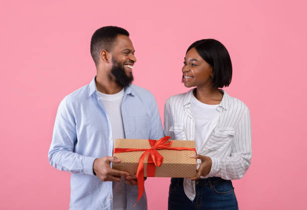 istock Passionate black couple holding gift box for Valentine's Day on pink studio background 1297776984