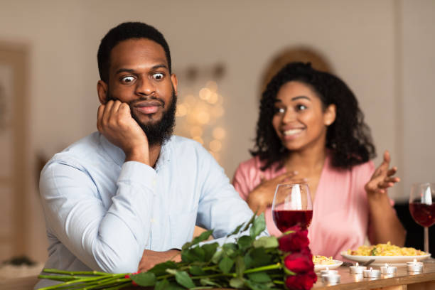 Black Man On Unsuccessful First Date In Restaurant Bad First Impression And Date Concept. Dissatisfied shocked black man listening to excited emotional obsessed woman talking, young couple sitting at table in cafe. Unpleasant conversation embarrassment stock pictures, royalty-free photos & images