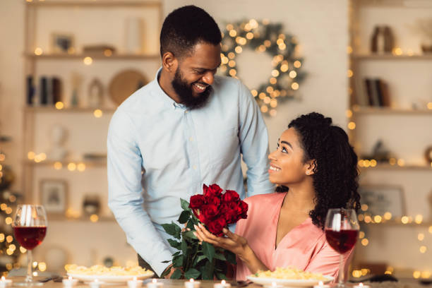 jeune homme noir de sourire donnant des roses rouges à la femme - anniversary couple rose black photos et images de collection