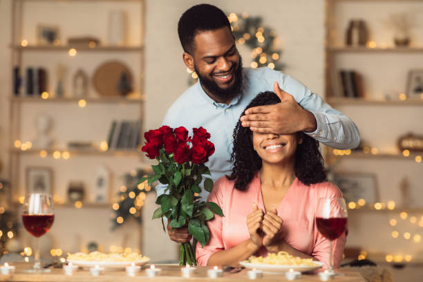 joven hombre negro dando flores a la mujer, cubriendo los ojos - valentines day food photography indoors fotografías e imágenes de stock