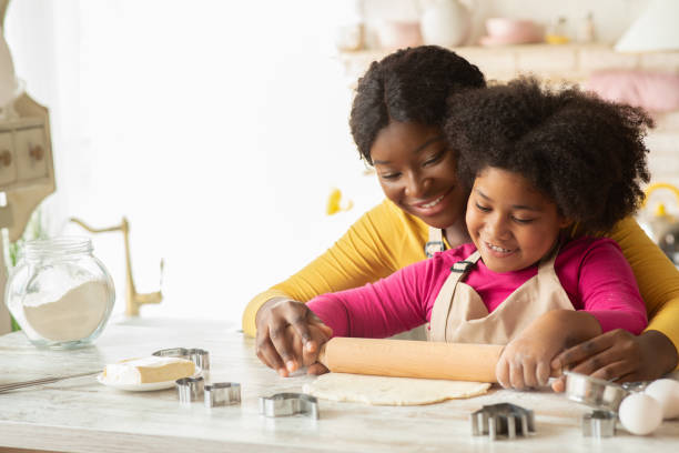 istock Happy black mom and her daughter rolling up dough together in kitchen 1297778739