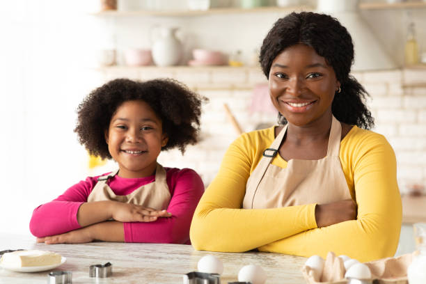 istock Happy Black Mom And Daughter In Aprons Sitting At Table In Kitchen 1297778824