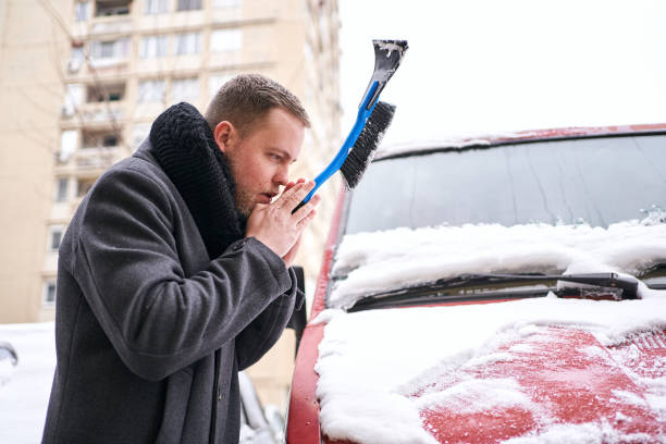 człowiek dmuchanie w rękę, więc może utrzymać ciepło podczas usuwania śniegu z jego samochodu z skrobaczka lodu - snow car window ice scraper zdjęcia i obrazy z banku zdjęć