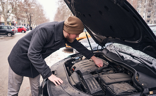 A man observing a car engine, after the car won't start on a cold winter day