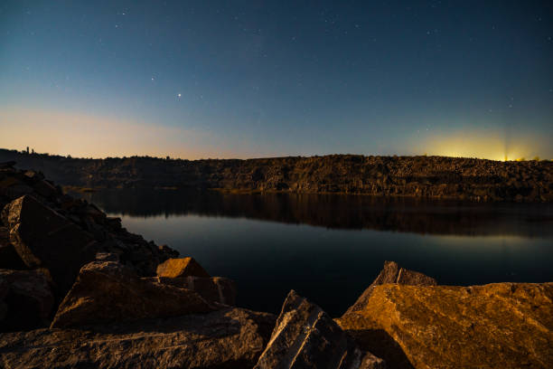 istock Old flooded stone quarry surrounded by stone waste from a mine work against a beautiful night sky 1297778996