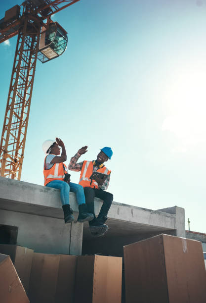 When your office feels like a playground Shot of a young man and woman sitting on top of a building at a construction site and giving each other a high five construction lunch break stock pictures, royalty-free photos & images