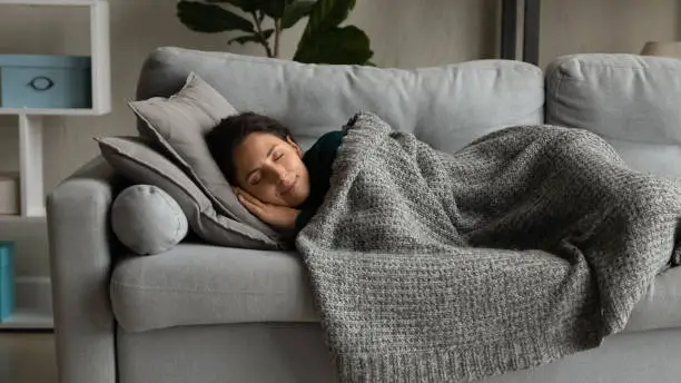 Photo of Happy young woman sleeping under blanket on sofa